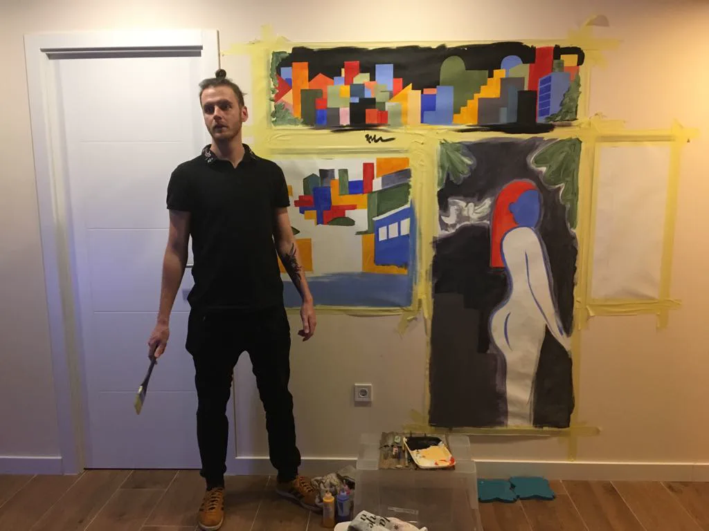 Nico Belico standing beside a large hand-painted wall composition